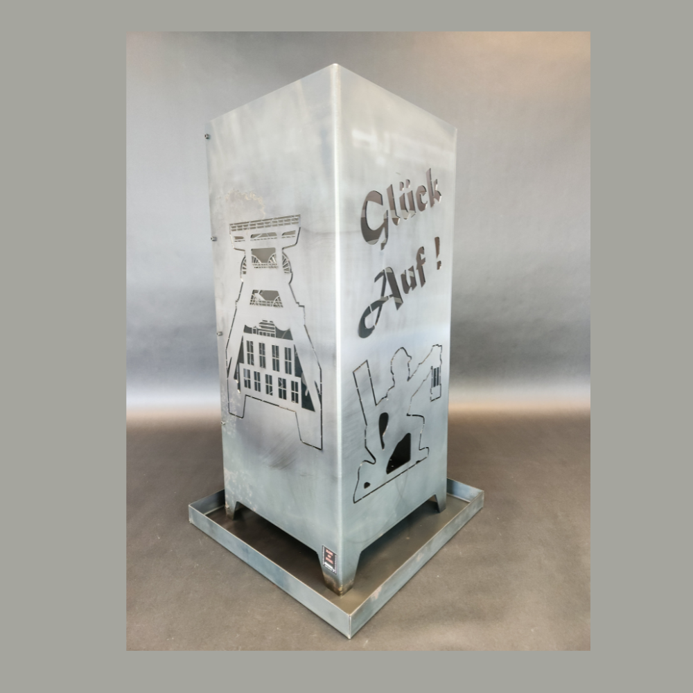 Feuersäule aus Stahl gefertigt in der hauseigenen Produktion. Abmessung 350 x 350 mm und 800 mm hoch. Motiv auf der einen Seite Gasometer, auf der anderen Seite der Schriftzug Glück auf darunter ein knieender Bergmann. Auf der Anderen Seite das Motiv: Dop