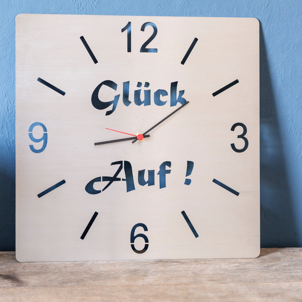 Edelstahluhr zum aufhängen an die Wand mit dem Schriftzug Glück auf.