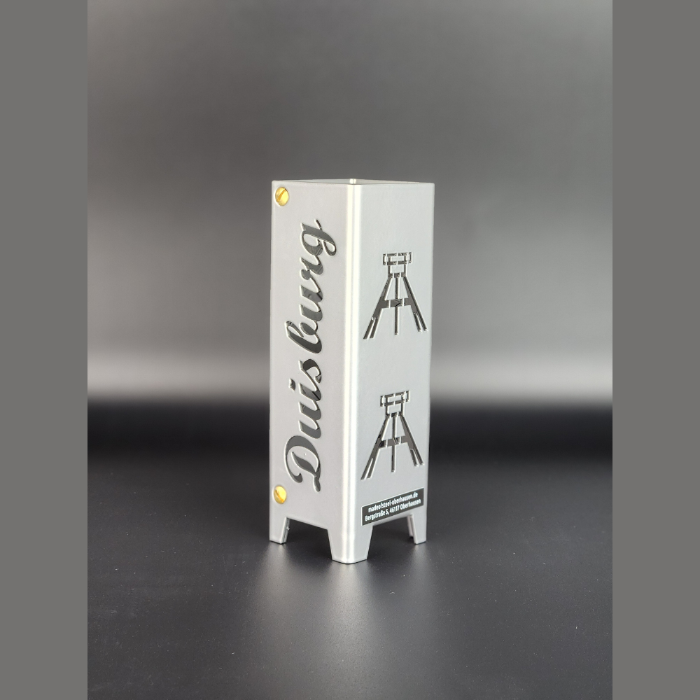 Teelicht aus hochwertigen Metall gefertigt und in brillant silber pulverbeschichtet. Schriftzug Duisburg und auf der anderen Seite Symbole Fördertürme, jeweils zwei Symbole übereinander. Für den Innenbereich geeignet.