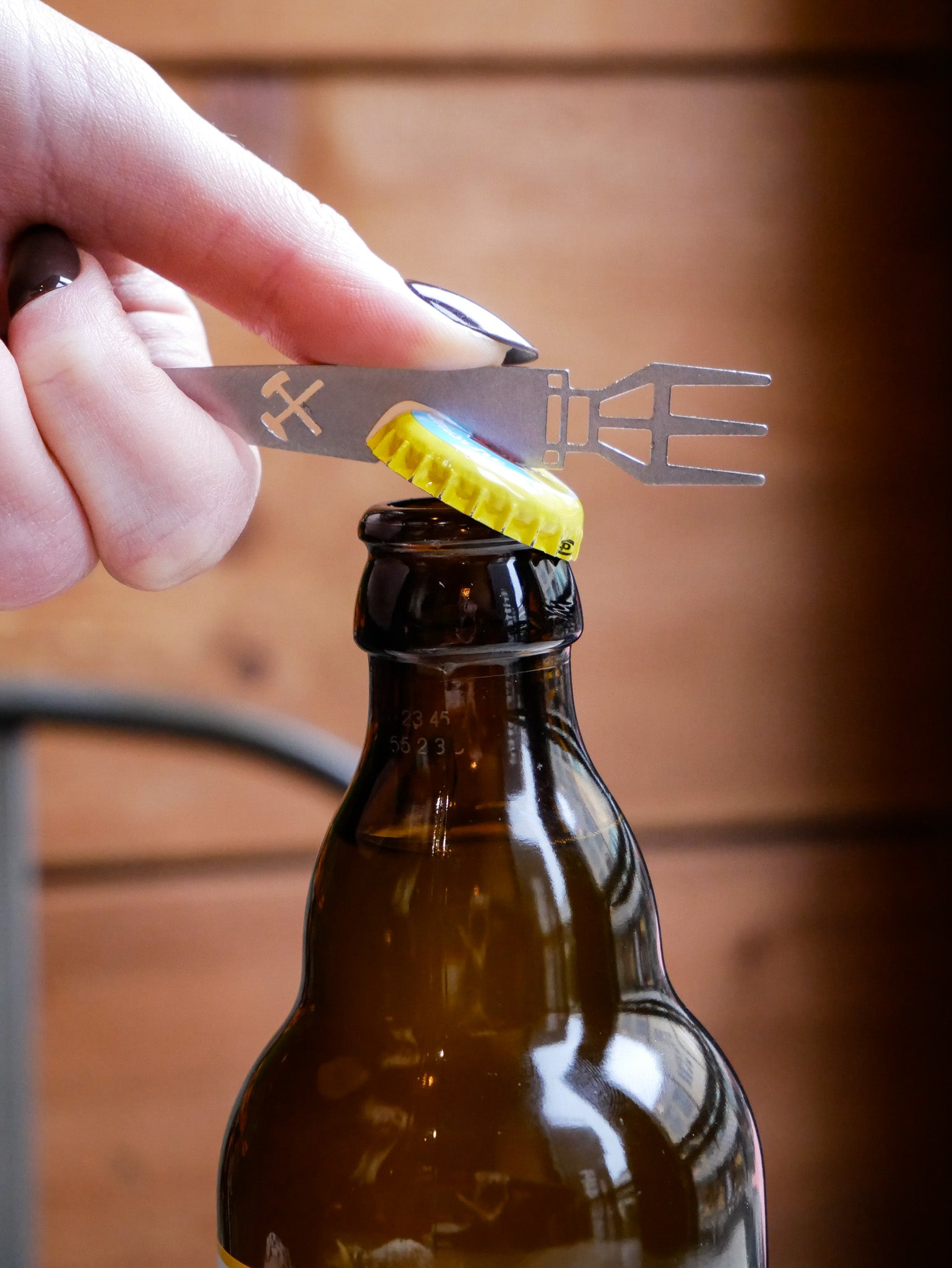 Eine Bierflasche wird mit dem PomBierPicker aus Edelstahl von Made of Steel Metalldesign by Viefhaus geöffnet. Tolles Snack-Tool mit Pommesgabel und integriertem Flaschenöffner, gefertigt in Oberhausen.