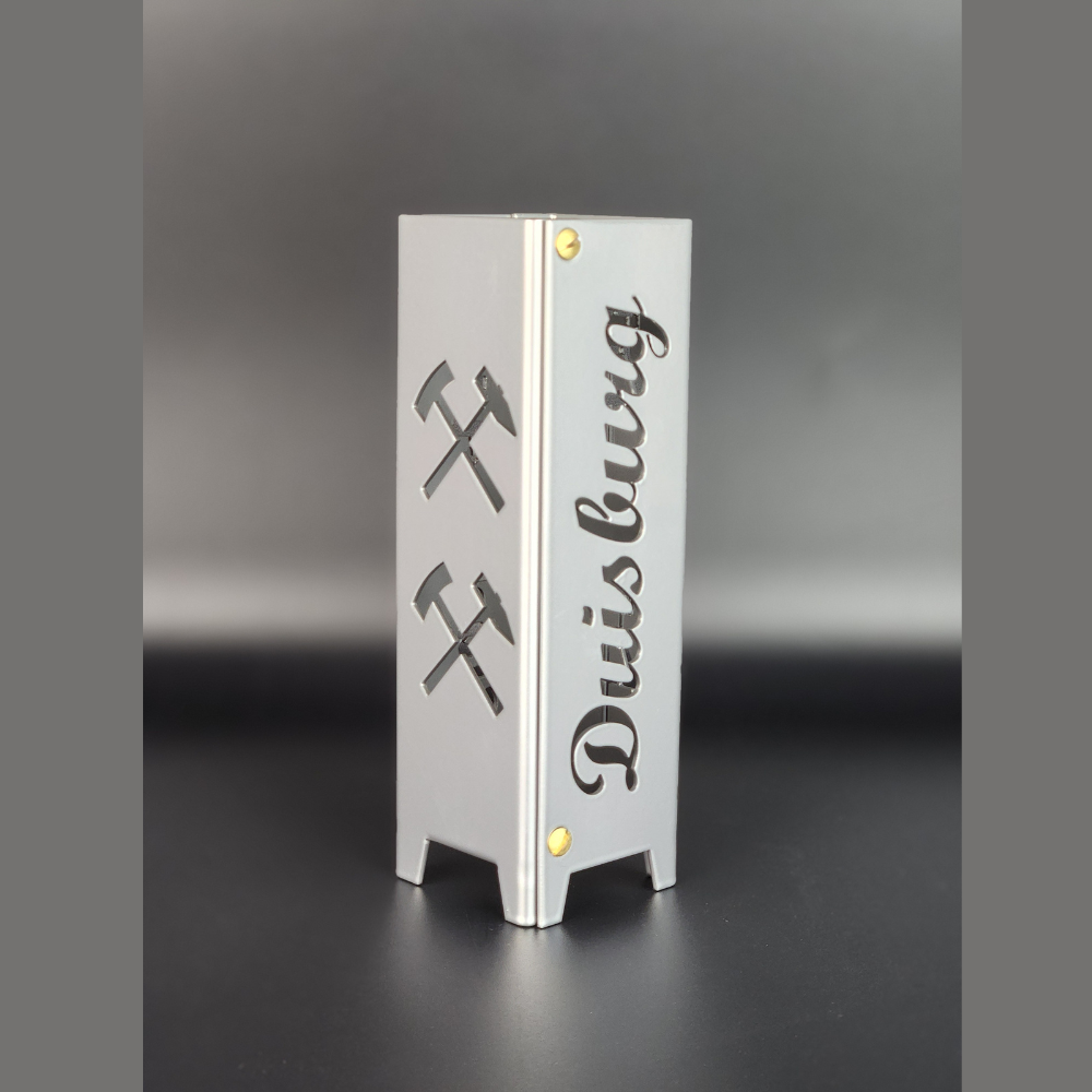 Teelicht aus hochwertigen Metall gefertigt und in brillant silber pulverbeschichtet. Schriftzug Duisburg und auf der anderen Seite Symbole Eisen und Schlägel, jeweils zwei Symbole übereinander. Für den Innenbereich geeignet.