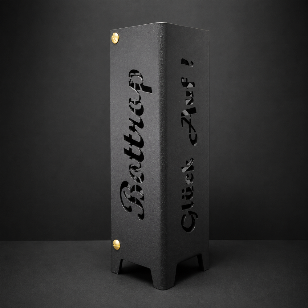 Schwarzes oder brillant silber pulverbeschichtetes Metall-Teelicht im Format 55 × 55 × 175 mm. Die vier Seiten zeigen die gelaserten Motive „Bottrop“, „Glück auf“, einen Förderturm sowie das Symbol Eisen und Schlägel. Das Windlicht erzeugt mit einem Teelicht stimmungsvolle Lichteffekte und eignet sich als Dekoration für den Innenbereich.
