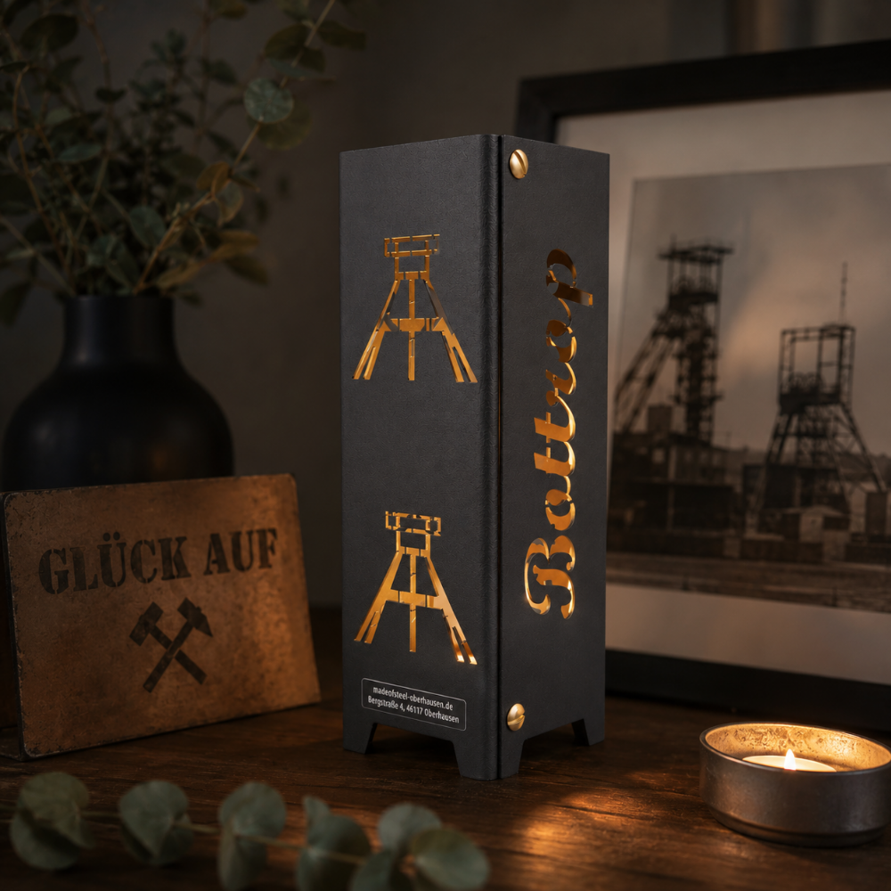 Schwarzes oder brillant silber pulverbeschichtetes Metall-Teelicht im Format 55 × 55 × 175 mm. Die vier Seiten zeigen die gelaserten Motive „Bottrop“, „Glück auf“, einen Förderturm sowie das Symbol Eisen und Schlägel. Das Windlicht erzeugt mit einem Teelicht stimmungsvolle Lichteffekte und eignet sich als Dekoration für den Innenbereich.